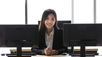 Beautiful Asian woman sitting alone and smile in office among computer screen