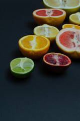 A variety of citrus fruits, cut in half, on a black copy space background, flat lay.