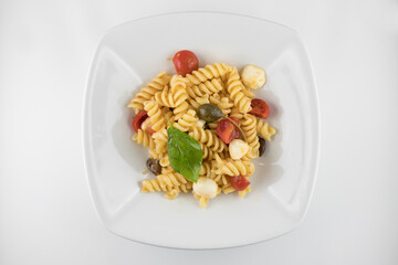 Piatto di pasta con pomodori, mozzarella, olive, capperi e basilico su sfondo bianco