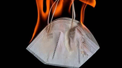 Burning Medical Mask on Black Background. The Coronavirus is Destroyed in a Fire, End of Covid-19 Restrictions.