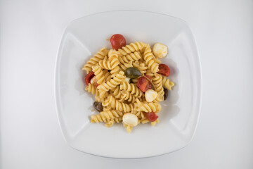 Piatto di pasta con pomodori, mozzarella, olive e capperi su sfondo bianco