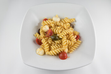 Piatto di pasta con pomodori, mozzarella, olive e capperi su sfondo bianco