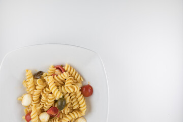 Piatto di pasta con pomodori, mozzarella, olive e capperi su sfondo bianco