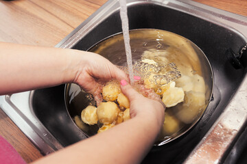Woman washing raw peeled potatoes under running water in the sink