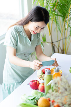 Asian woman using her phone to take a picture of her plant-based meal