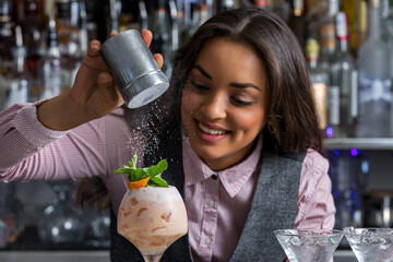 Happy female barkeeper adding powdered sugar to cocktail