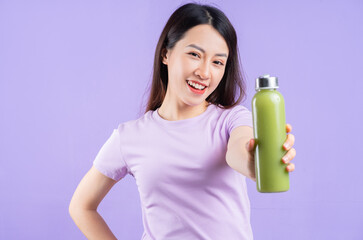 Young Asian woman holding a bottle of juice on purple background