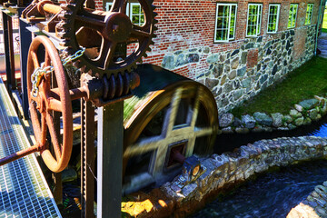 Wooden mill wheel of a historical water mill turns in the flowing water of the streaming brook ,...