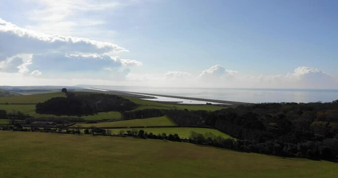Aerial shot flying over fields and grass with a beach and coast in the background