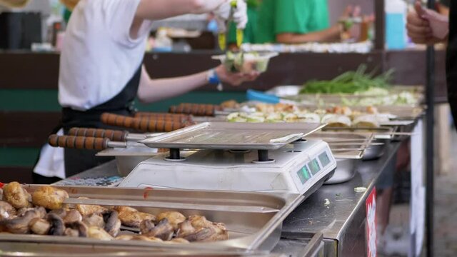 Buyer Pay Cash to Street Food Vendor per Kebabs, Salad in a Lunch Box. Trade Fast Food on Open Stalls. Weighing on scales. Fried vegetables, barbecue lie on counter. Food truck. Takeaway food. Zoom.