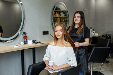 A young girl visited a hairdresser. The woman is drinking coffee. Hair Styling.
