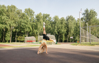 A blonde girl in a sports uniform on the playground performs an exercise wheel