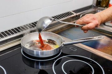 Chef mentre aggiunge del sugo di pomodoro in una padella con olio e frutti di mare