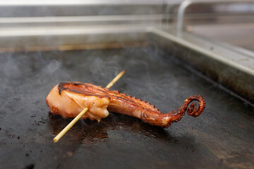 Tentacolo di polpo infilzato con uno spiedo in cottura su piastra rovente