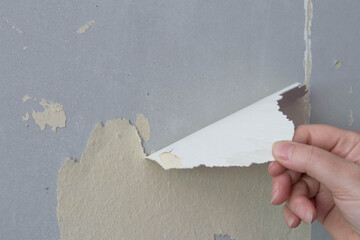 Hand pulling peeling old wallpaper off a plasterboard wall.