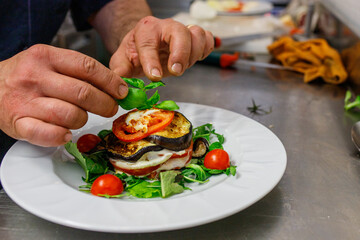 Chef mentre guarnisce una millefoglie di melanzane, mozzarella e pomodoro con del basilico fresco