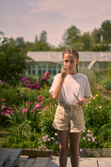 country house garden a young girl with pigtails in a white T-shirt stands against a background of greenery and there is a marshmallow just fried on the fire