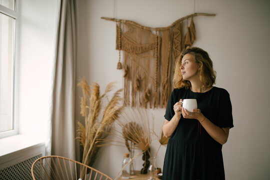 Young woman drinking tea or coffee in a cozy room with bohemian interior.