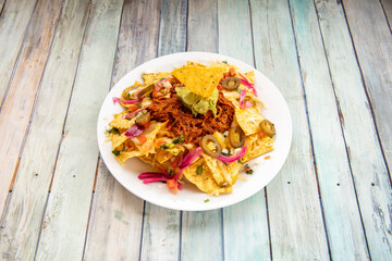 Mexican corn nachos with avocado guacamole, cochinita pibil meat and sliced jalapenos on white plate
