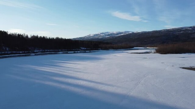 flying over snow patch covered river shore with clean cold melting water running through the river and mighty forest and snowy peak mountain in the backdrop, aerial video