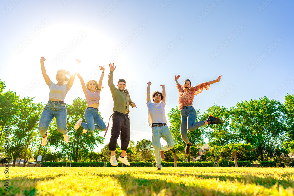 Wall mural backlit photography of multiracial group of college students jumping high with open up arms smiling 