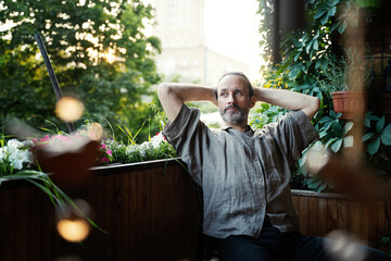 Attractive mature man relaxing and enjoying the fresh air while sitting on balcony on a sunny day