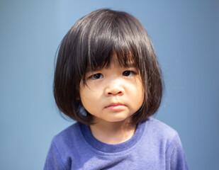 Naklejka premium A headshot portrait of a cheerful baby Asian woman, a cute toddler little girl with adorable bangs hair, a child wearing a blue sweater smiling and looking to the camera.