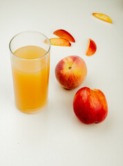 side view of peach juice in a glass and sweet nectarines on white background