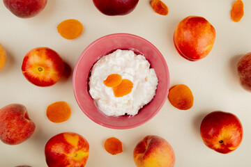 top view of cottage cheese in a bowl and fresh sweet nectarines and peaches with dried apricots on white background