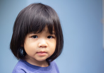 Naklejka premium A headshot portrait of a cheerful baby Asian woman, a cute toddler little girl with adorable bangs hair, a child wearing a blue sweater smiling and looking to the camera.