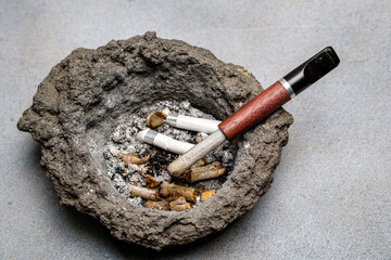 Cigarette holder and cigarette butts in an old dirty volcanic lava ashtray. Close-up. Selective focus.