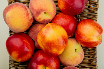 Fototapeta na wymiar top view of fresh ripe peaches and nectarines on a wicker tray on white background