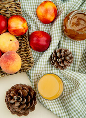 top view of fresh ripe peaches and nectarines on a wicker tray with a glass of peach jam and glass of juice on plaid fabric background