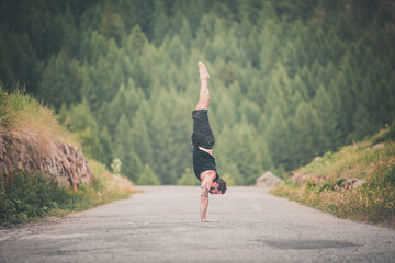 Giovane uomo in verticale in montagna in mezzo alla natura. Posizione Yoga, Verticale.