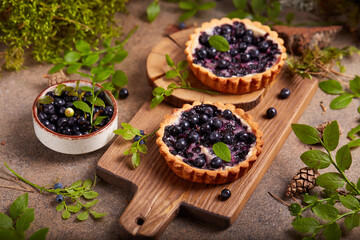 Mini tarts with blueberries and sour cream filling. Sweet homemade dessert with wild forest berries.