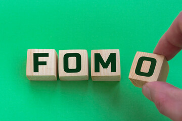 FOMO, acronym for Fear of Missing Out in wooden alphabet letters isolated on green background