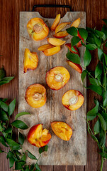 top view of halves of fresh ripe peaches on a wooden cutting board with green leaves on rustic background