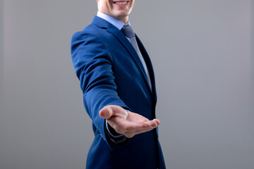 Smiling caucasian businessman reaching his hand, isolated on grey background