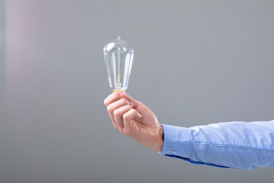 Midsection of caucasian businessman holding light bulb, isolated on grey background