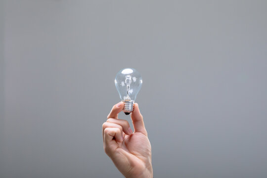 Close up of caucasian businessman holding light bulb, isolated on grey background