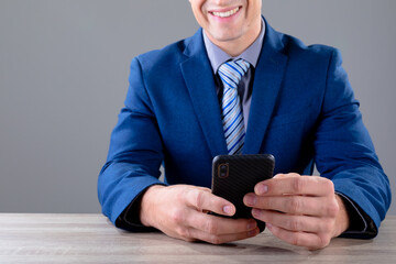 Smiling caucasian businessman using smartphone, isolated on grey background