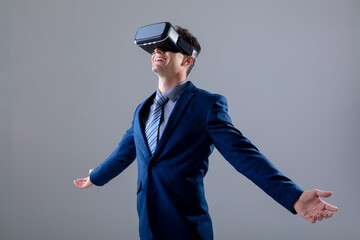 Caucasian businessman wearing vr headset widening his arms, isolated on grey background - Powered by Adobe