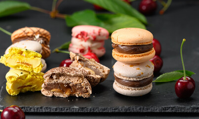 stack of multicolored macarons and ripe red cherries on black wooden background