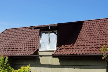 one white attic window on a brown tiled roof of a house against a blue sky