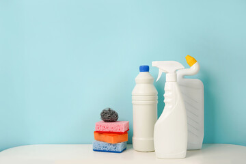 Set of white bottles of different cleaning procucts and sponges on blue background with empty space for text