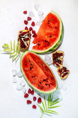 Summer background: slices of fresh watermelon with pomegranate fruit, raspberry, ice, palm leaf on white background