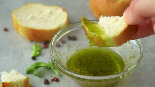 Female hands dip piece of fresh french baguette in pesto sauce with olive oil. Snack with basil sauce. Close up