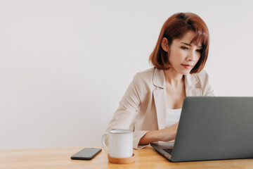 Asian working woman is using laptop on the office desk with white background.