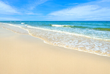 Summer sand beach with ocean waves and blue sky background.