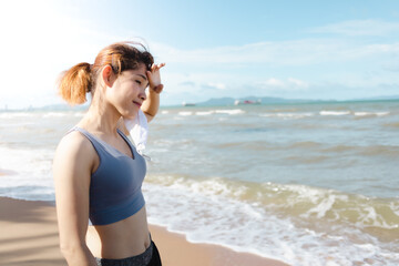 Fototapeta na wymiar Asian woman take off mask and rest after finish jogging by the beach in summer.